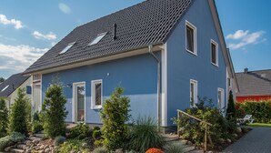 Ein modernes, zweistöckiges Haus mit geneigtem Dach, zahlreichen Fenstern und einem gepflegten Garten mit verschiedenen Pflanzen und einem Kiesweg.