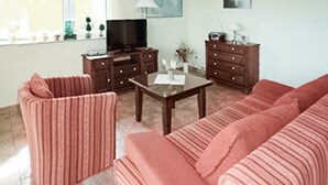 Un salon comprenant un canapé, un fauteuil, une table basse, un meuble pour la télévision et des armoires.