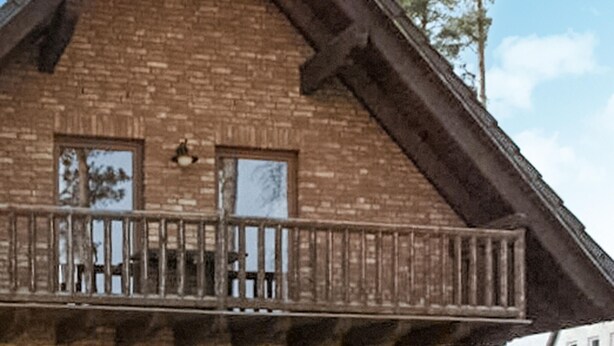 Un balcon en bois avec une balustrade, un mur en briques et deux fenêtres.