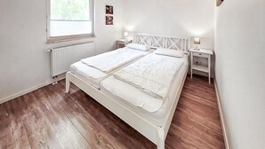 Ein Doppelbett mit weißer Bettwäsche in einem Zimmer mit Holzboden und weißen Wänden.