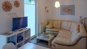 Ein Wohnzimmer mit Flachbildfernseher, einem beigen Sofa, einem Glastisch und einer kleinen Pflanze.