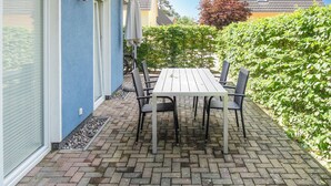 Eine Terrasse mit Tisch und Stühlen, eine blaue Wand und ein Heckenstreifen.