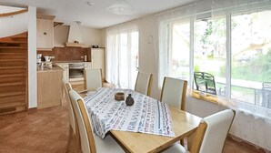 Un comedor con una mesa y sillas de madera, una cocina al fondo y vistas al exterior a través de amplios ventanales.