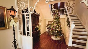 Una imponente escalera con balaustrada blanca, un árbol de Navidad y una lámpara de estilo vintage.