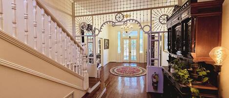 A grand staircase leading to a spacious foyer with a decorative railing, a chandelier, and a large wooden cabinet with plants.