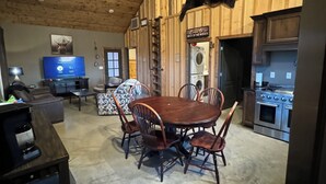A rustic interior with a wooden ceiling, a dining area with a round table and chairs, a television, and a kitchen with a stove. - Duck hunting cabin (Newport)
