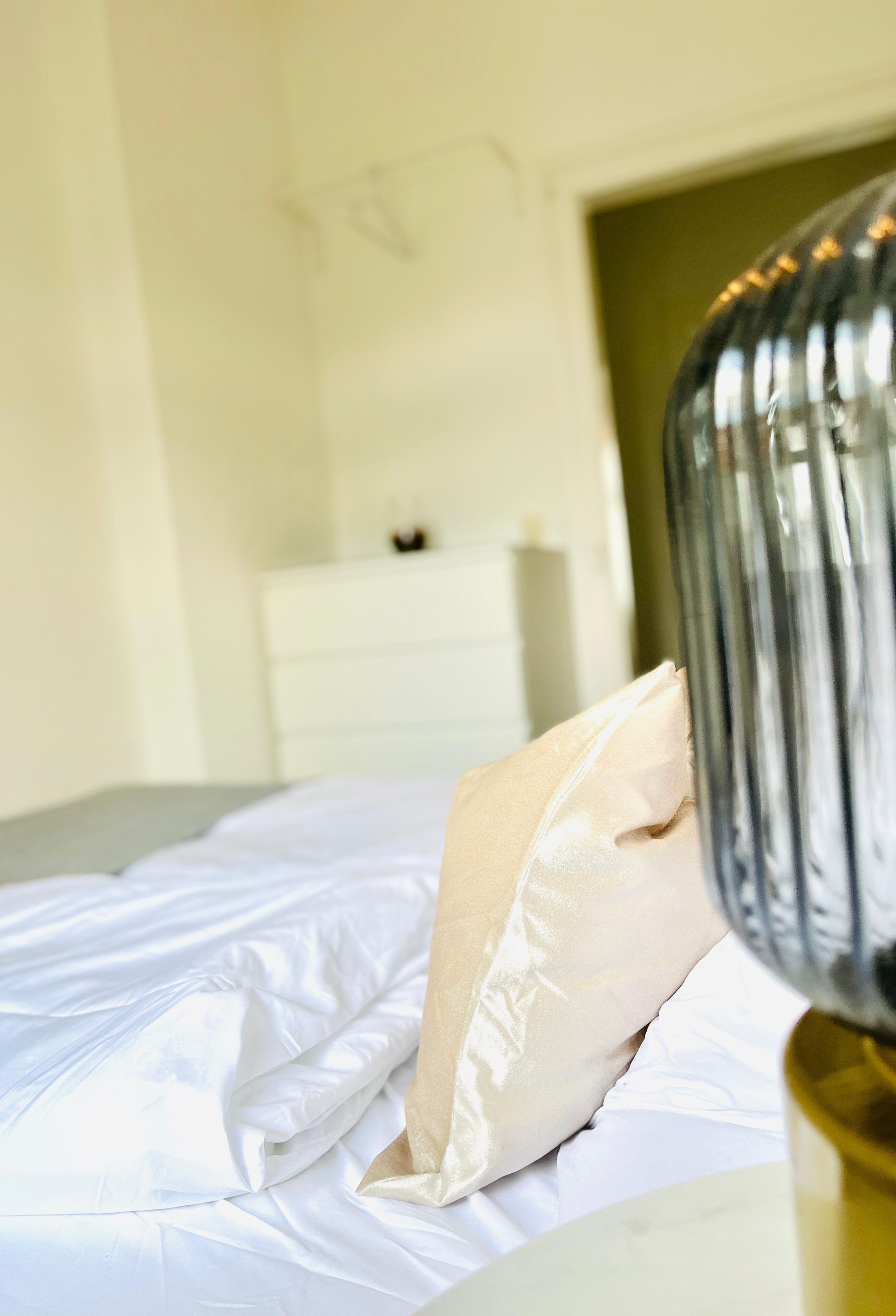 A neatly made bed with white linens and a beige pillow.