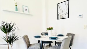 Ein Essbereich mit einem runden Tisch, vier Stühlen, einer Zimmerpflanze und Wanddekorationen, darunter ein gerahmtes Bild und ein Thermostat.