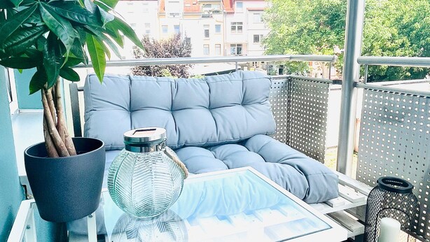 Ein Balkon mit bequemen Sitzmöglichkeiten, einem Glastisch, einem Blumentopf und einer dekorativen Laterne.