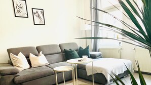 Ein modernes Wohnzimmer mit einem grauen Sofa, einem kleinen runden Tisch und einer großen Pflanze.