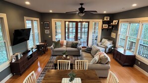 A spacious living room with a large wooden dining table, two sofas, and a television.