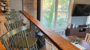 A kitchen with a long wooden counter, several chairs, a stove, and a window with a view of trees.