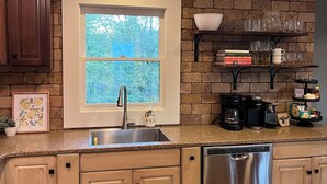 A kitchen with a window, built-in cabinets, a stainless steel dishwasher, and a coffee maker.