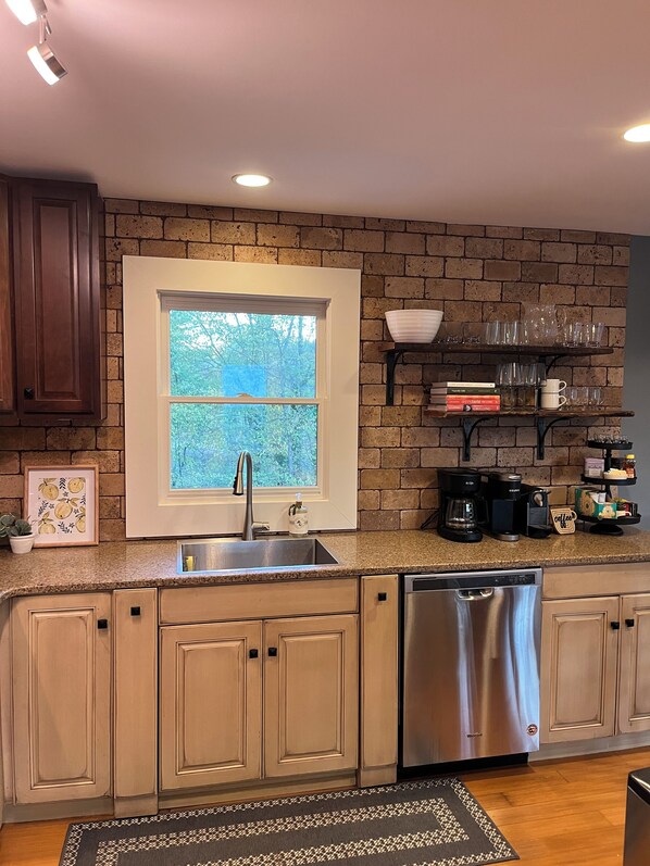 Una cocina con ventana, armarios empotrados, lavavajillas de acero inoxidable y cafetera.
