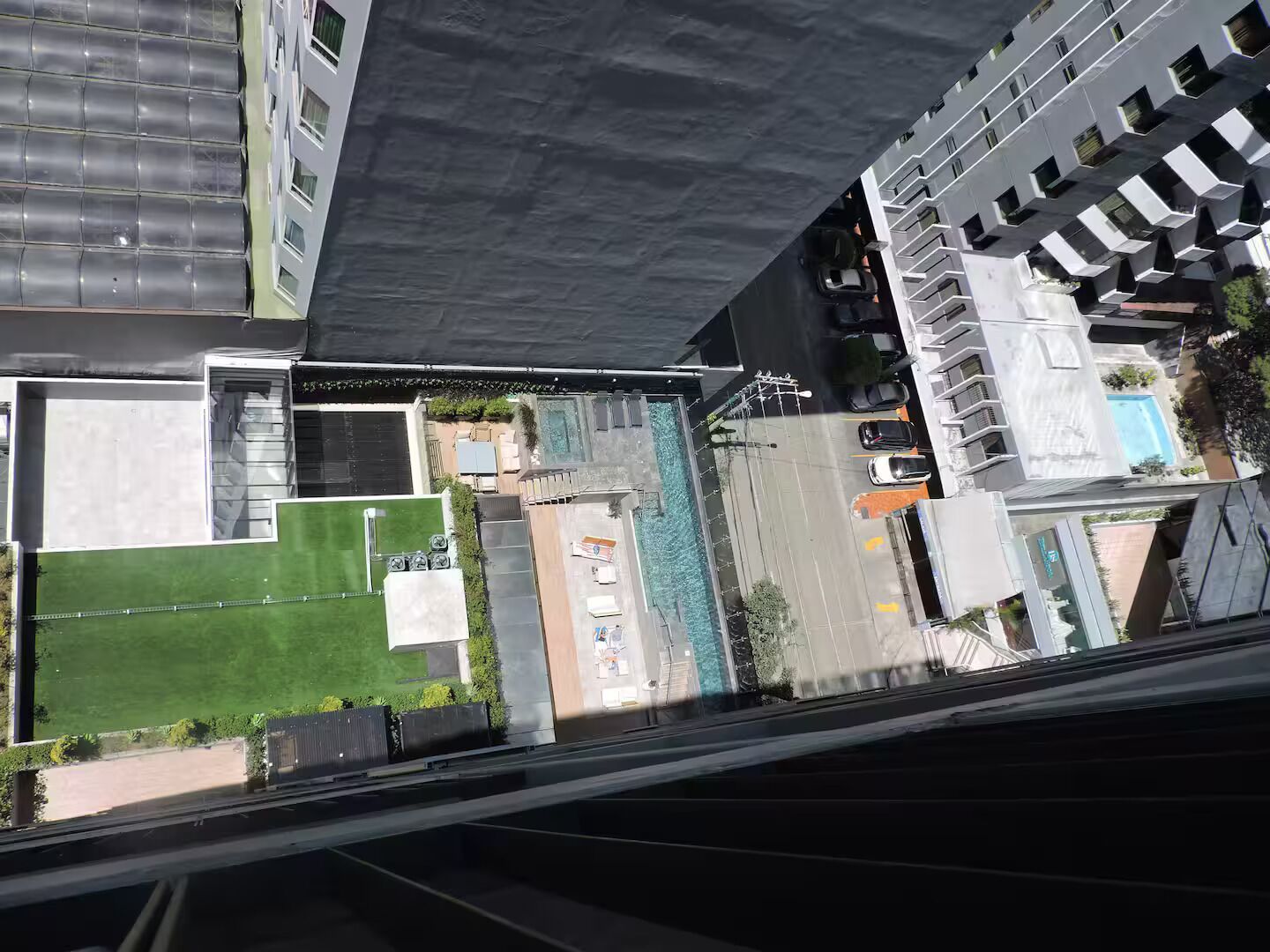 Un edificio de gran altura con piscina en la azotea, césped verde y zona de estacionamiento.