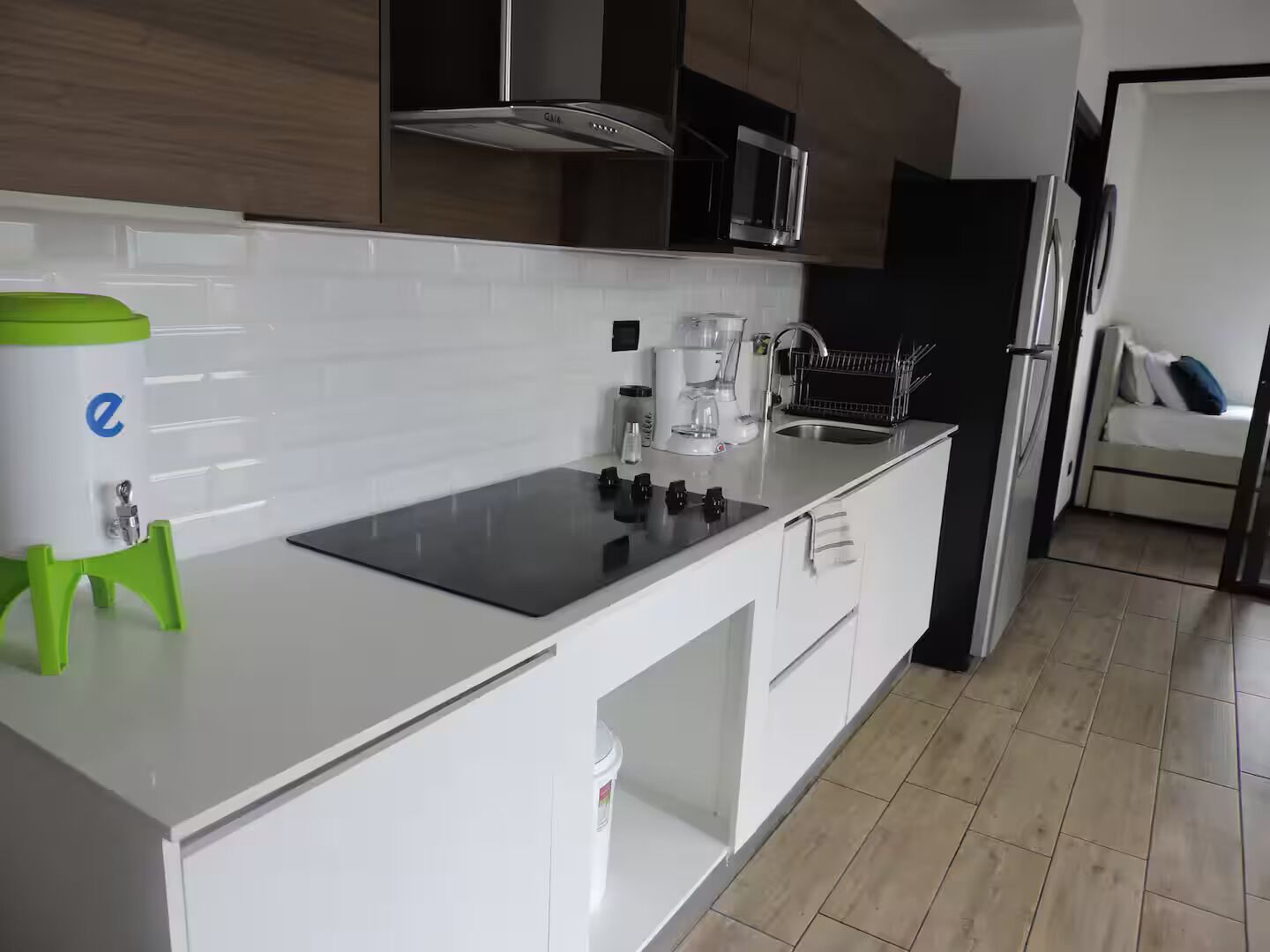 Una cocina moderna con armarios blancos, una estufa negra, una cafetera y un dispensador de agua.