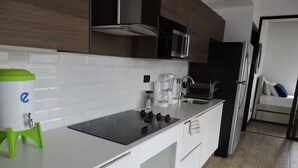 Una cucina moderna con mobili bianchi, un piano cottura nero, una macchina da caffè e un dispenser d'acqua.
