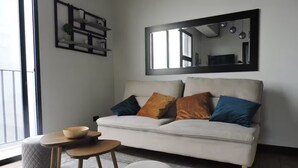 Un soggiorno moderno con un divano bianco, due poggiapiedi, un piccolo tavolino in legno e una mensola decorativa.