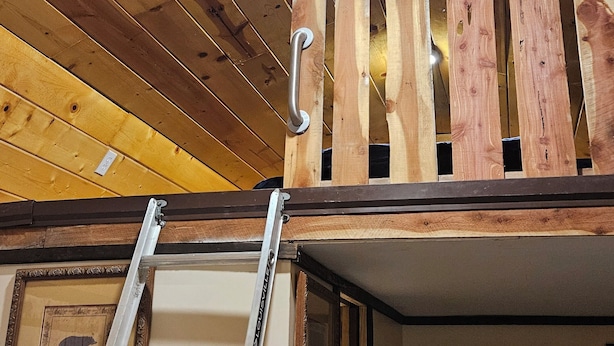 A loft-style room with a slanted ceiling, a ladder, and a wooden wall.