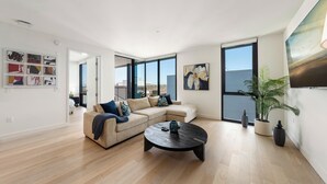 A modern living room with a sectional sofa, a round coffee table, and large windows offering a view of the city. - The Sapphire Nest' Luxury Condo Walk to Beach & Pier Rooftop Pool, Gym Parking (Santa Monica)