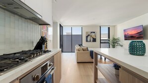 A modern kitchen with a gas stove, wooden cabinets, and a large window. - The Sapphire Nest' Luxury Condo Walk to Beach & Pier Rooftop Pool, Gym Parking (Santa Monica)