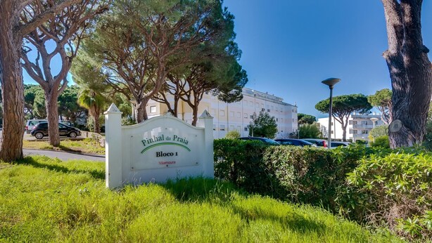 En skylt med texten ”Pinhal da Praia Bloco 1 Vilamoura”, och i bakgrunden syns en byggnad och parkerade bilar.