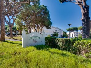 A sign for 'Pinhal da Praia Bloco 1 Vilamoura' with a view of a building and parked cars in the background. - Pine Retreat (Vilamoura)