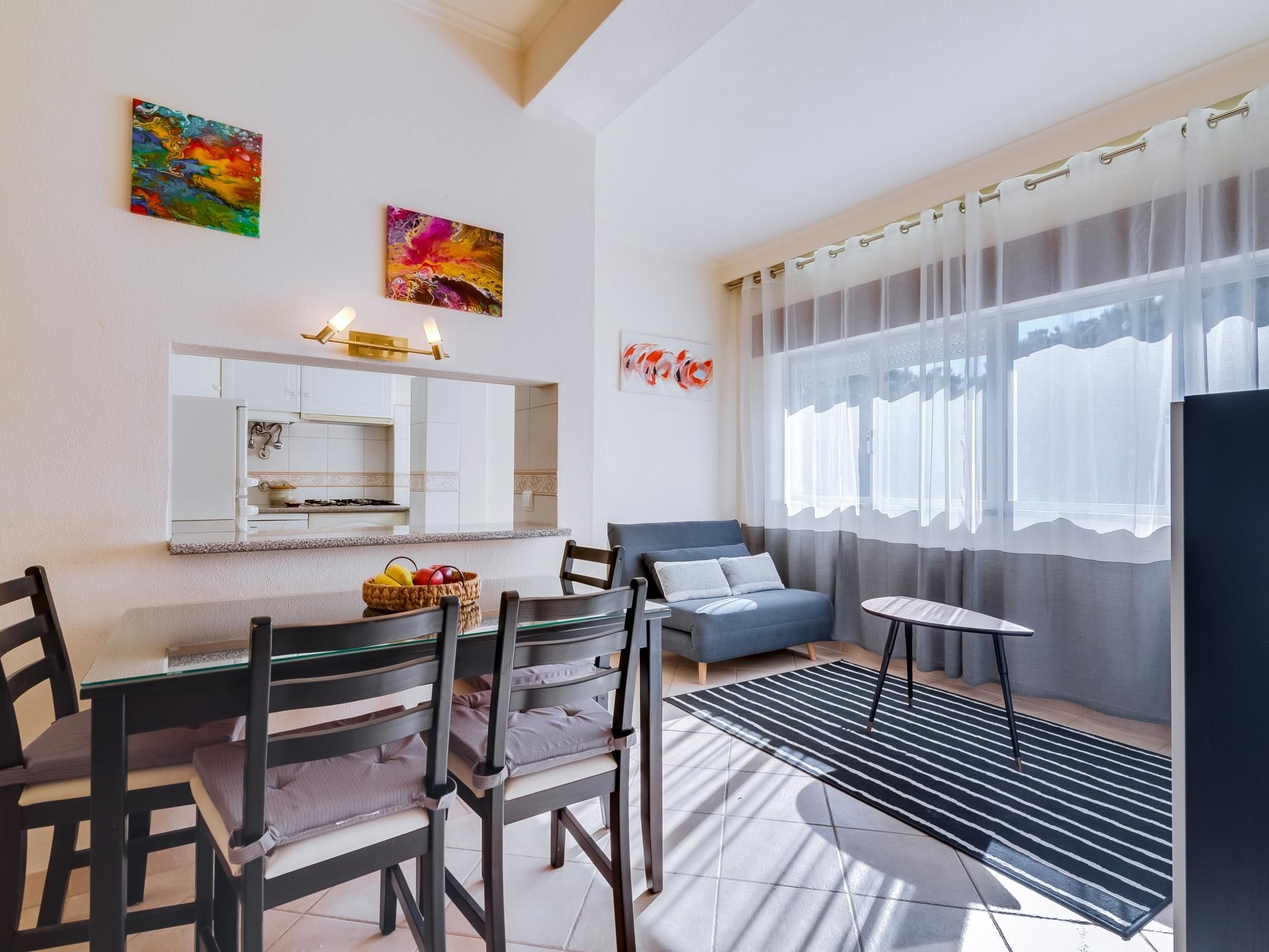 A modern living room with a dining area, a sofa, a table, and a kitchen visible in the background.