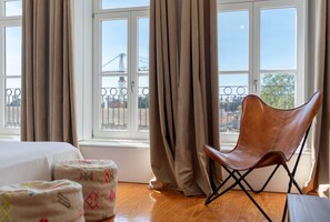 Ein Zimmer mit einem Bett, einem braunen Ledersessel und Blick auf eine Brücke durch große Fenster.