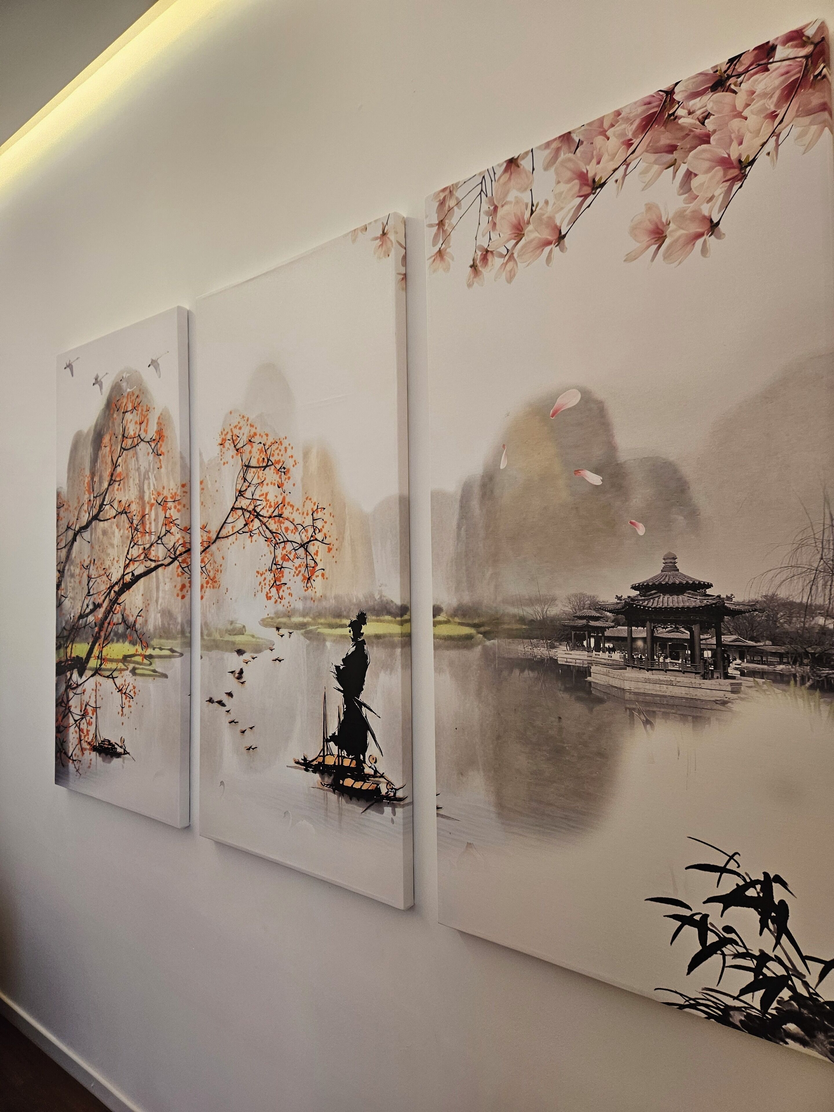 Un mur orné de trois tableaux représentant des paysages paisibles, avec des montagnes, des arbres et un pavillon traditionnel.