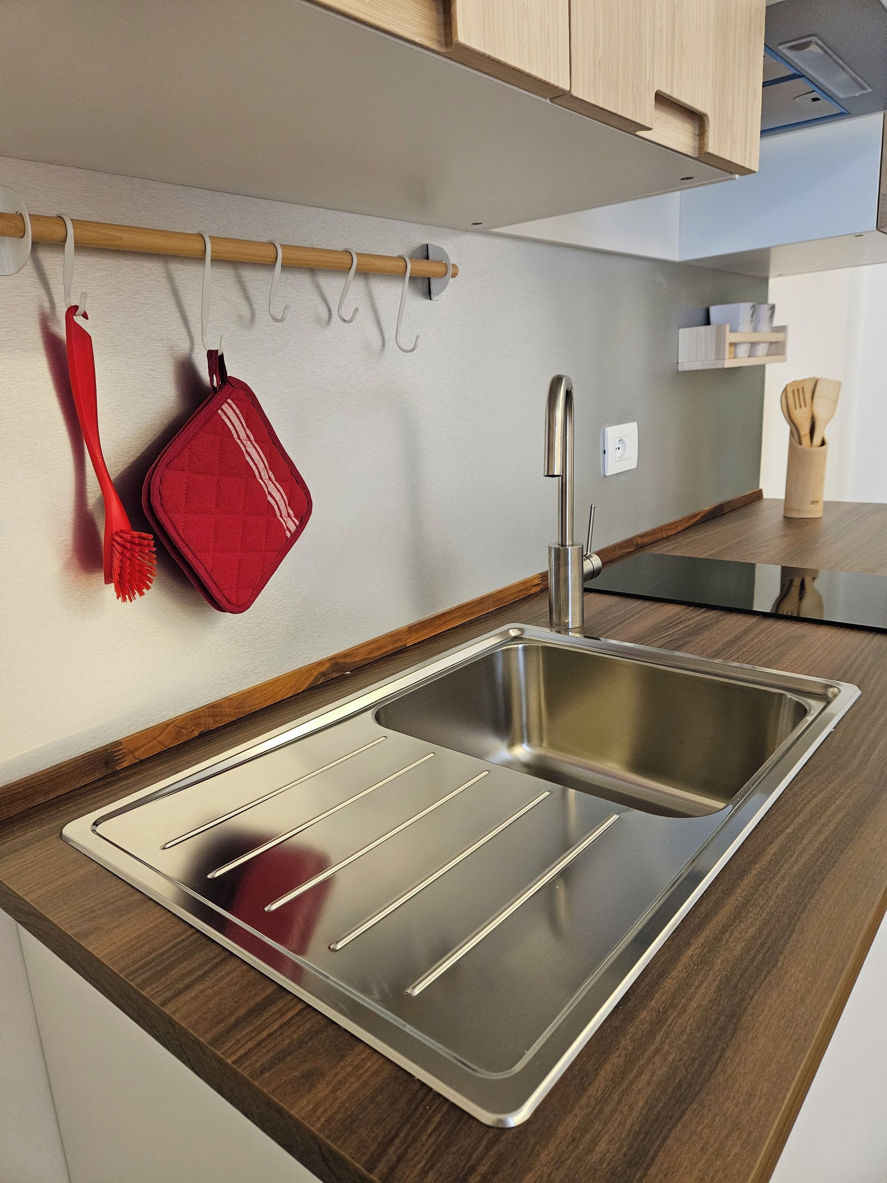 A modern kitchen with a stainless steel sink, wooden countertop, and a red utensil holder.