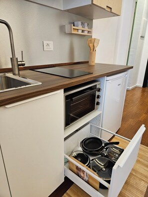 A compact kitchen with a built-in oven, a sink, and a drawer with cookware.
