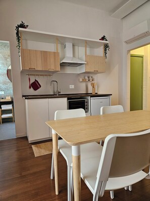 A compact kitchen with white cabinets, a built-in oven, and a dining area with a wooden table and white chairs.