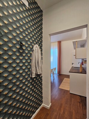 A modern interior with a patterned wallpaper, a hallway leading to a dining area, and a kitchen with a countertop and sink.