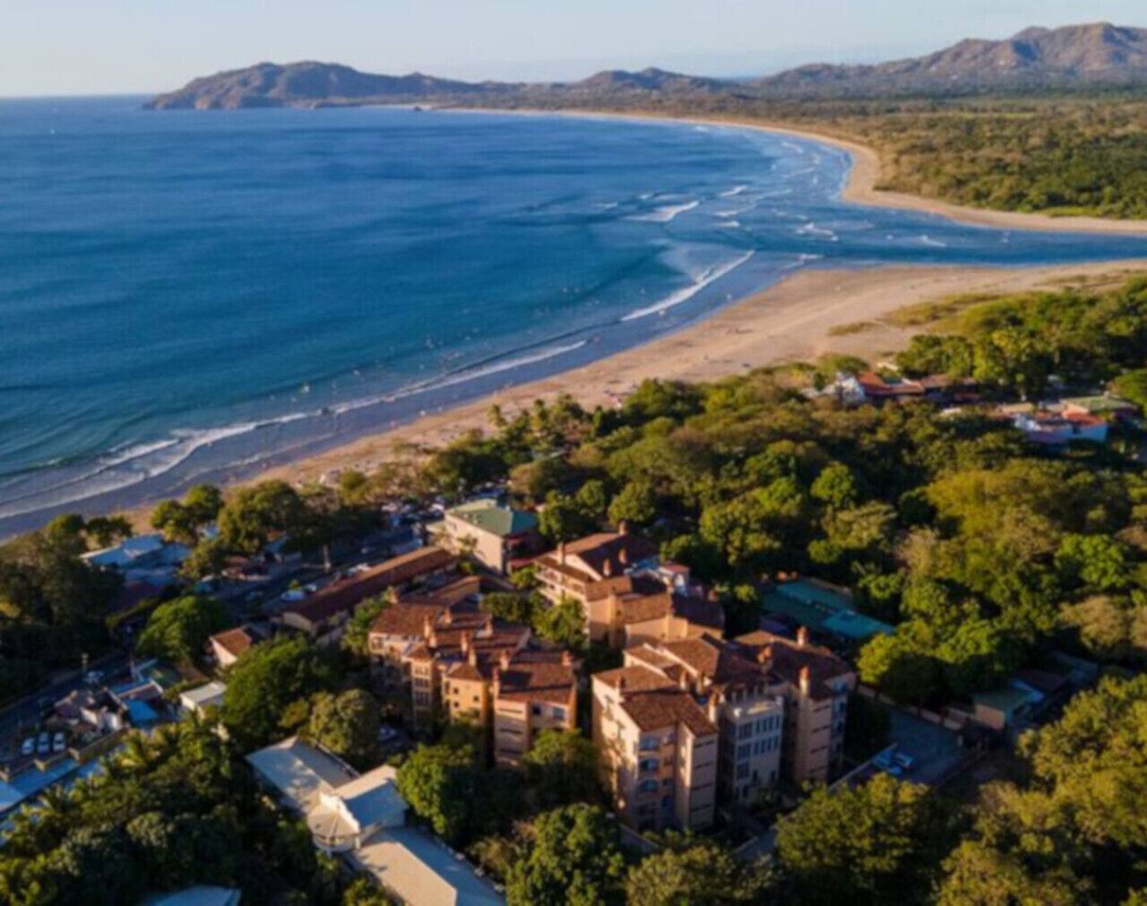 Une vue aérienne d’une ville côtière, avec un imposant ensemble de bâtiments entouré d’une végétation luxuriante et donnant sur une plage.