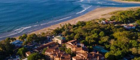 Une vue aérienne d’une ville côtière, avec un imposant ensemble de bâtiments entouré d’une végétation luxuriante et donnant sur une plage.
