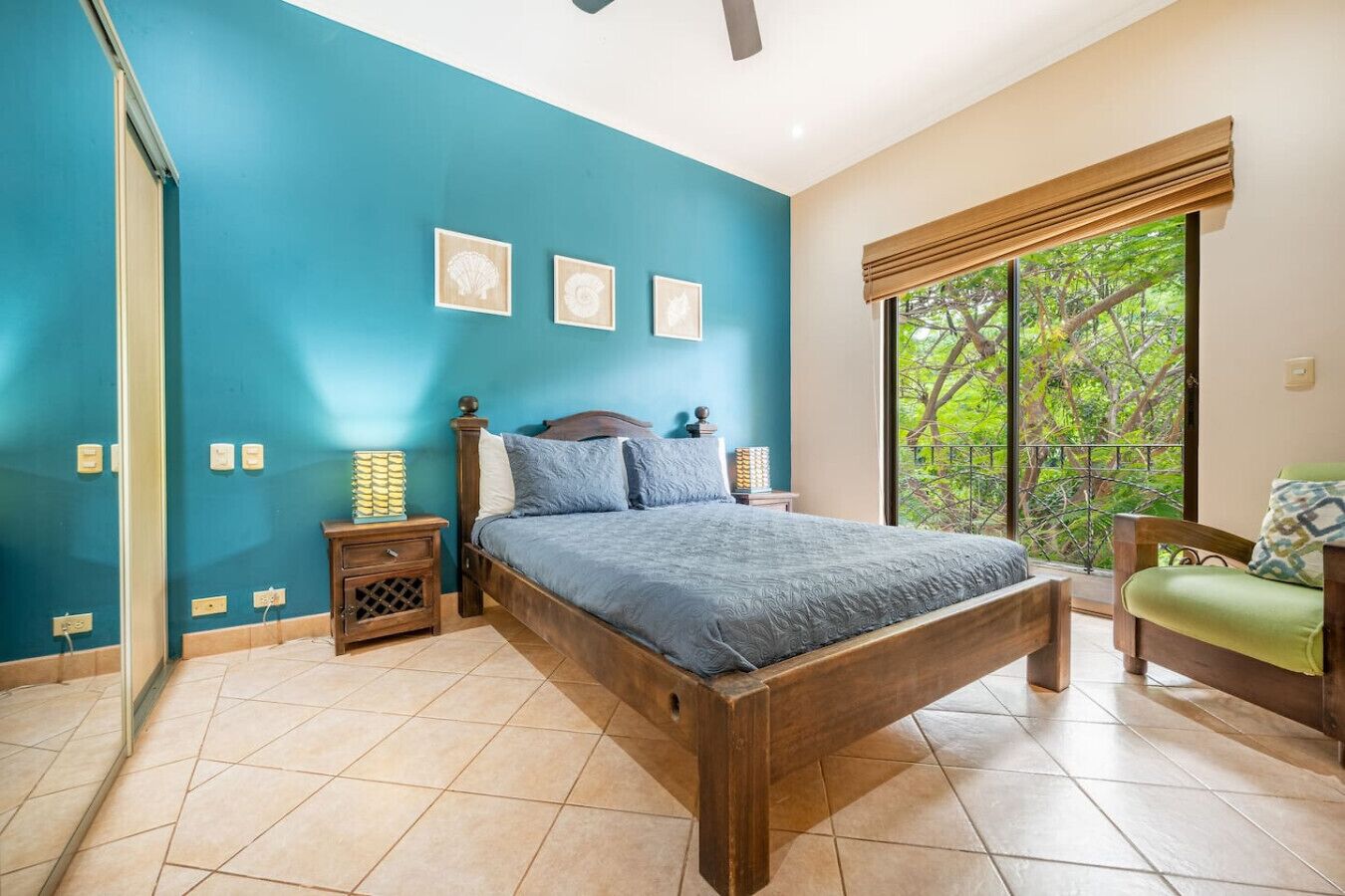 Ein Schlafzimmer mit einem hölzernen Bett, türkisfarbenen Wänden, einem Fenster mit Blick auf Bäume und einem grünen Sessel.
