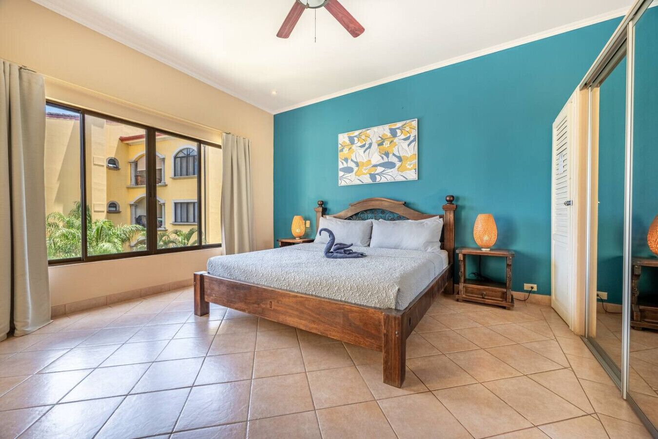 Un dormitorio con una cama grande, un ventilador de techo, vistas al exterior y un cuadro en la pared.