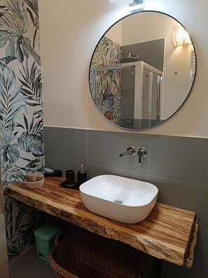 Une salle de bain avec un miroir rond, un lavabo blanc et un meuble-lavabo en bois.