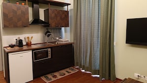 Een compacte keuken met een ingebouwde oven, een kleine koelkast en houten kastjes.
