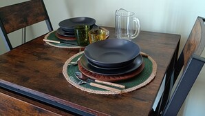 Een eettafel gedekt met borden, een karaf en bestek, omringd door stoelen.