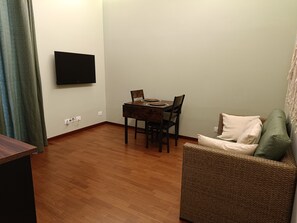 Une petite pièce meublée, comprenant une table à manger, des chaises, un téléviseur fixé au mur et un canapé en osier.