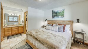 Ein Schlafzimmer mit einem großen Bett, einem Holzkopfteil, Nachttischlampen, einem Nachttisch und einem an der Wand hängenden Gemälde.