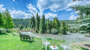 Ein Picknickbereich am Flussufer mit einer Bank, zwei Stühlen und einem Tisch mit einem Blumentopf.