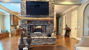 Una chimenea de piedra con un televisor de pantalla plana en la parte superior, una mesa de centro de madera al frente y vistas al área de la cocina.