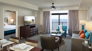Hotelkamer met een bed, een televisie, een balkon met uitzicht en een zithoek met een tafel en stoelen.