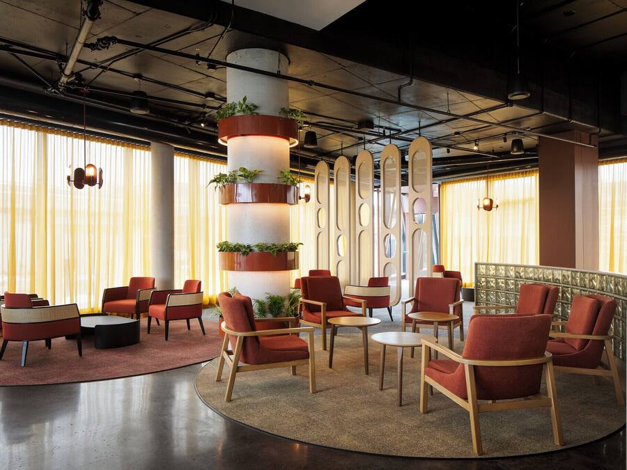 A lobby with round tables and chairs, a central pillar with plants, and a reception desk.