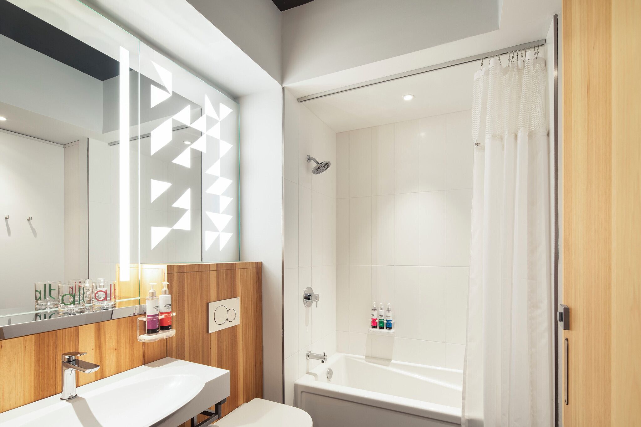 A modern bathroom with a wooden vanity, a large mirror, a shower with a glass door, and a bathtub.