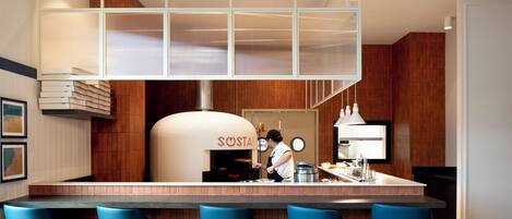 A modern kitchen with a pizza oven, bar seating, and a person preparing food.
