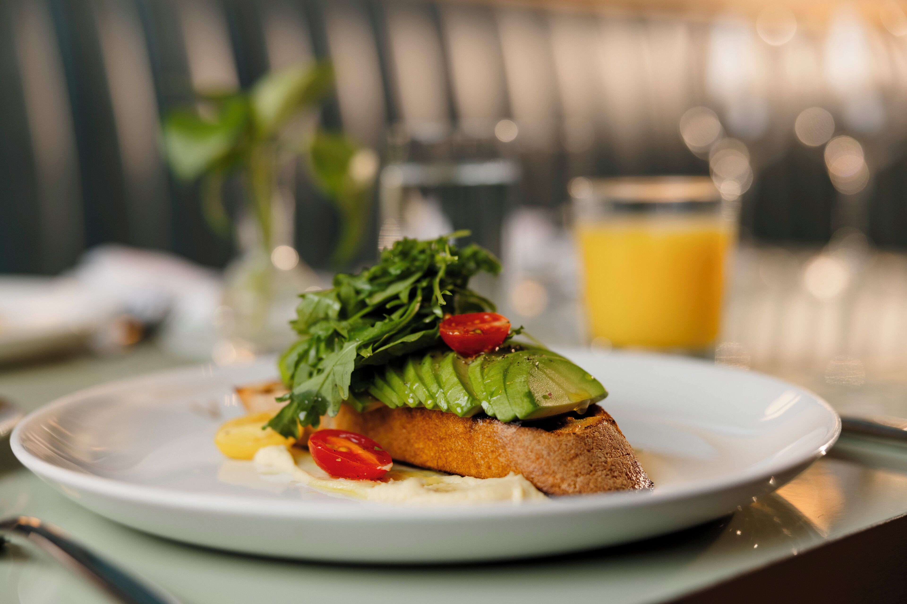 Un plato con un sándwich, un vaso de jugo de naranja y un pequeño jarrón con plantas.